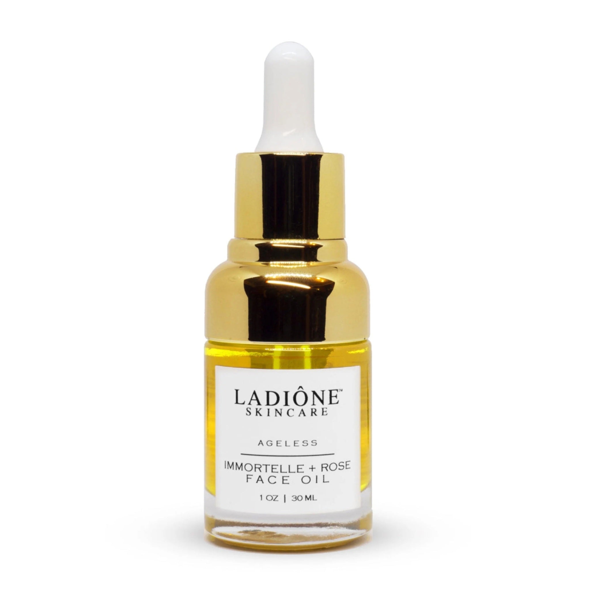 A clear glass bottle with a gold cap containing face oil, labeled 'LADIONE SKINCARE AGELESS IMMORTELLE + ROSE FACE OIL 1 oz / 30 ml'.