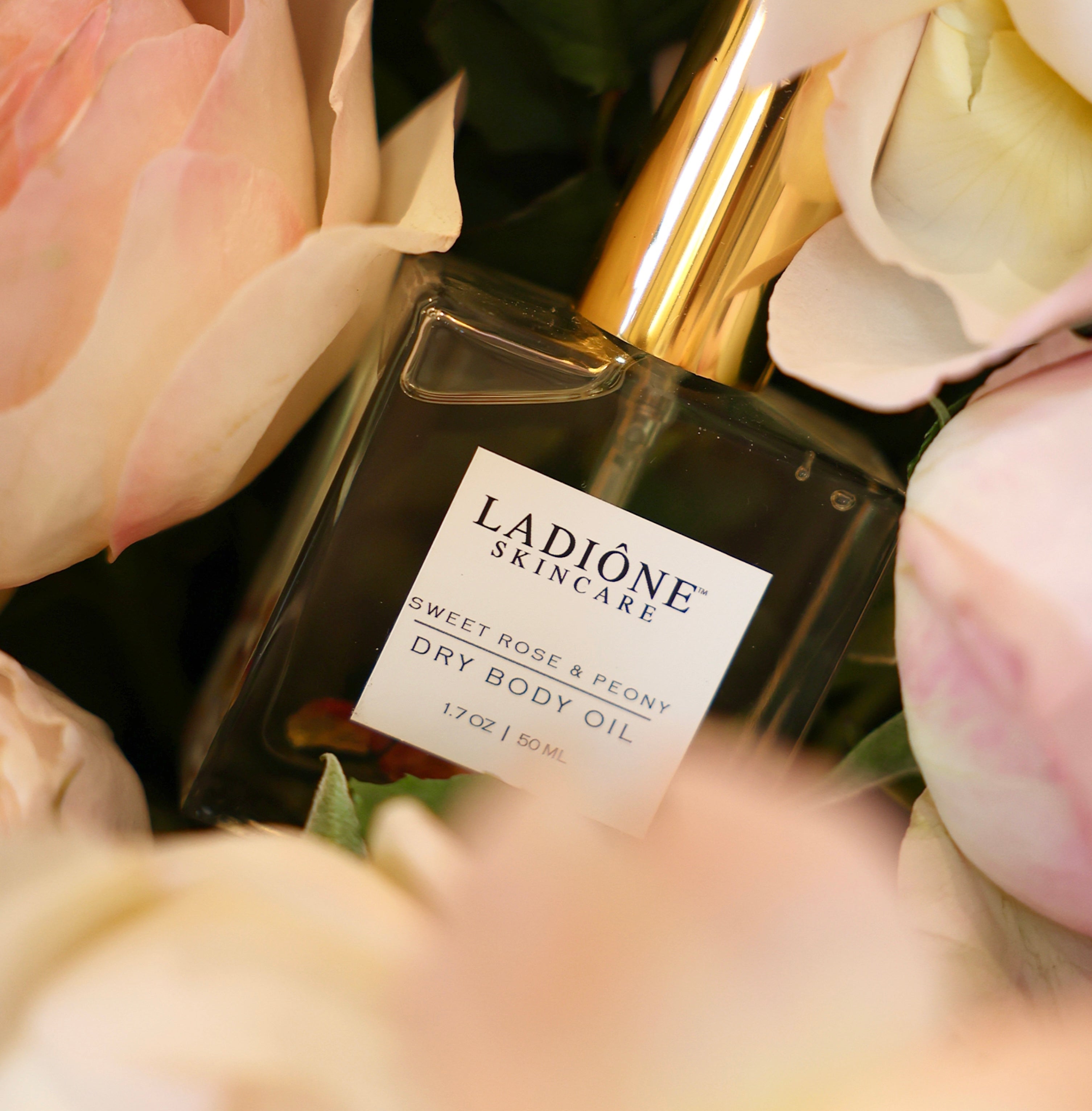 Ladiéne Skincare dry body oil bottle with a gold cap surrounded by pink roses.