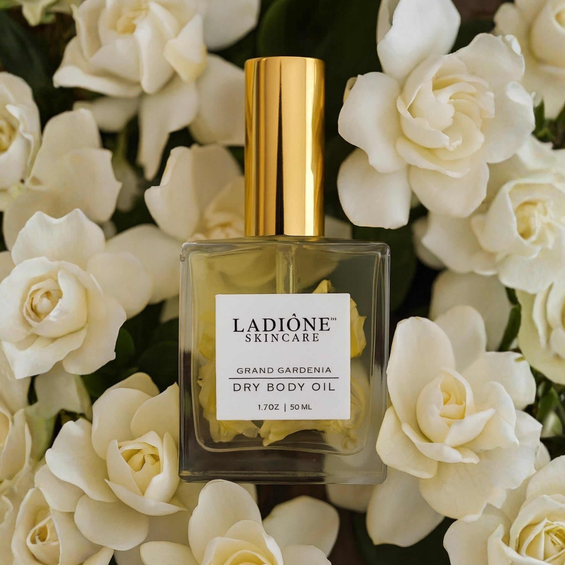 Ladione Skincare dry body oil bottle with gold cap on a background of white flowers