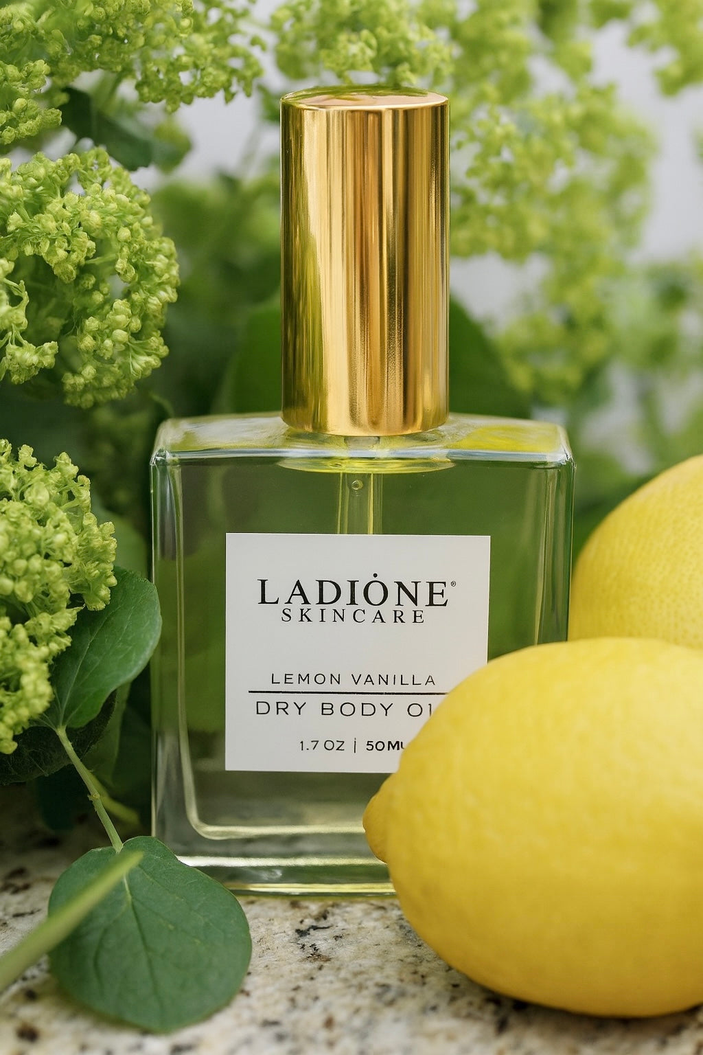 Ladiéne Skincare Lemon Vanilla dry body oil bottle with gold cap and lemons on a green leafy background